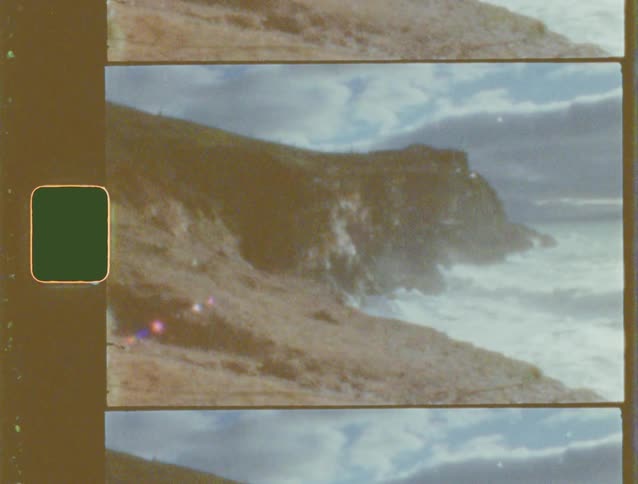 A vintage film scan captures a rugged and dramatic coastline with powerful waves crashing against the cliffs
