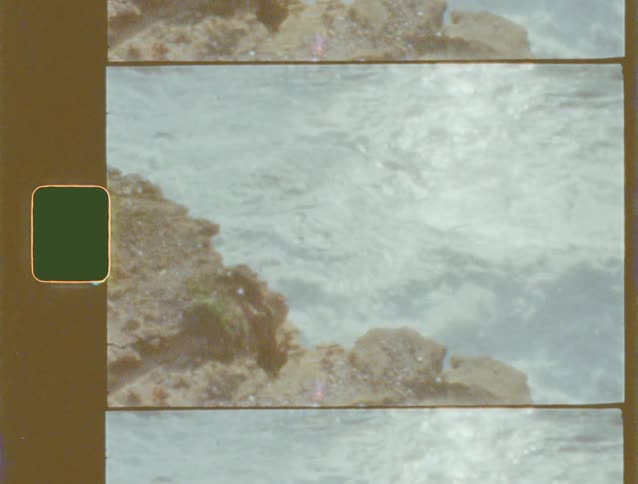 An authentic Super 8mm film shot of tranquil ocean waves gently washing over a rocky shoreline