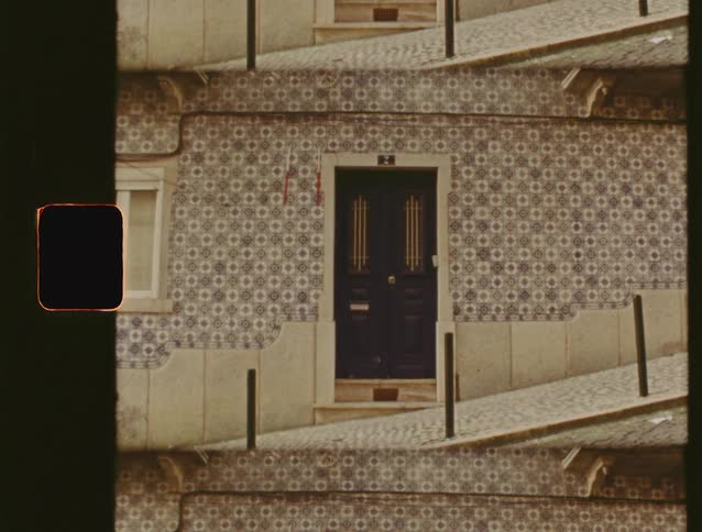 Vintage film captures the charming facade of a Portuguese building, adorned with traditional azulejo tiles on a sloped cobblestone street