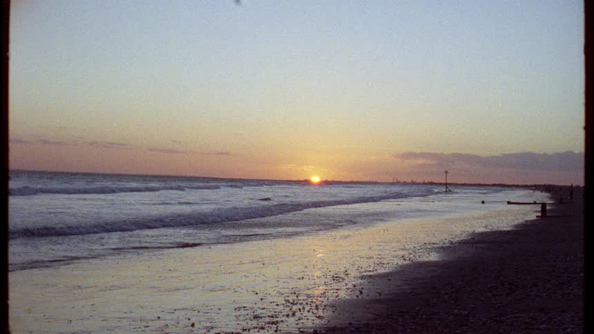 Vintage Super 8 footage captures a beautiful golden sunset over a tranquil ocean beach