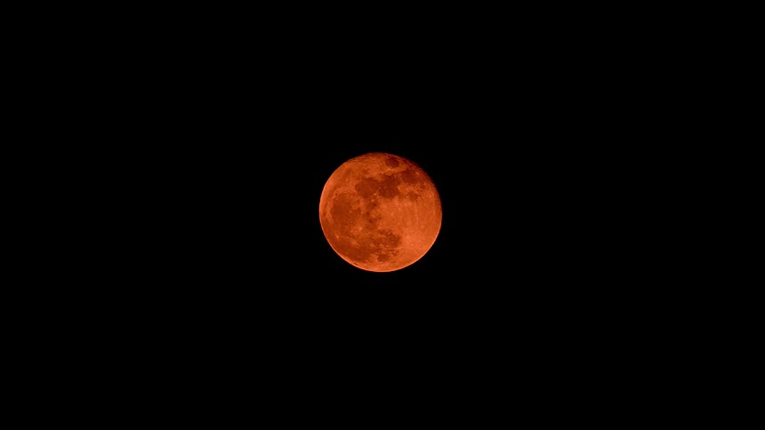 A close-up view of a vibrant red blood moon during a total lunar eclipse, glowing brightly against the pitch-black night sky