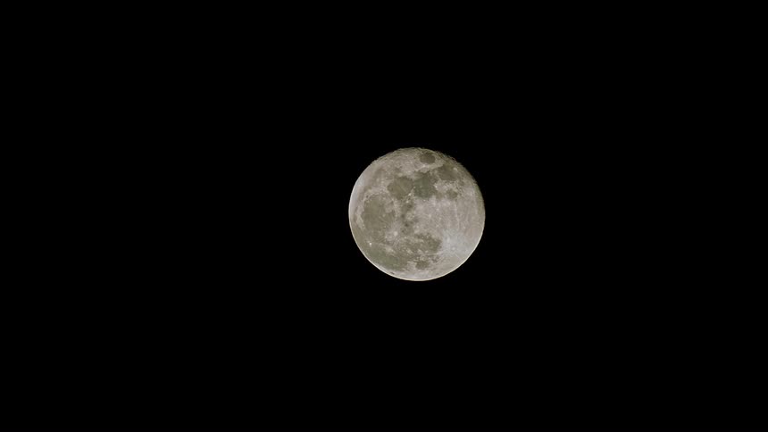 A detailed close-up time-lapse of a full moon ascending through the dark night sky
