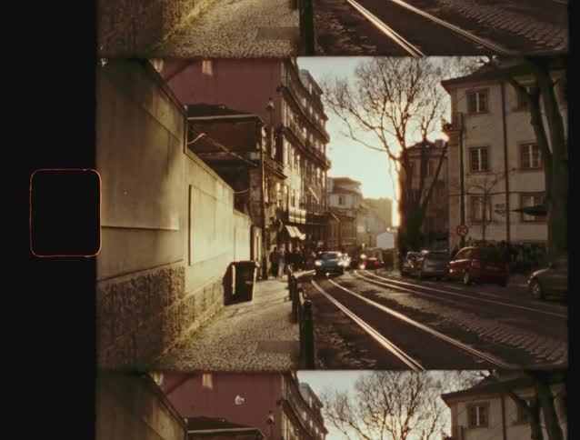A city street with tram tracks and historic buildings is bathed in warm sunset light in this vintage film-style shot