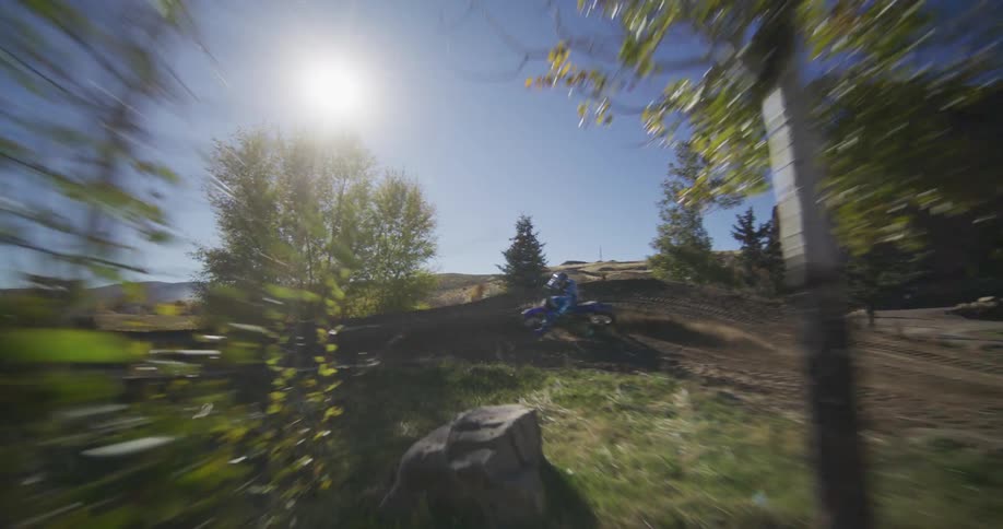 Dynamic follow shot of a motocross rider racing up a dirt hill on a beautiful sunny day