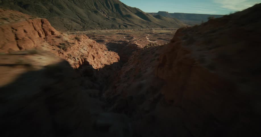A breathtaking first-person aerial flight reveals the dramatic, sun-drenched ridges of a vast desert canyon landscape