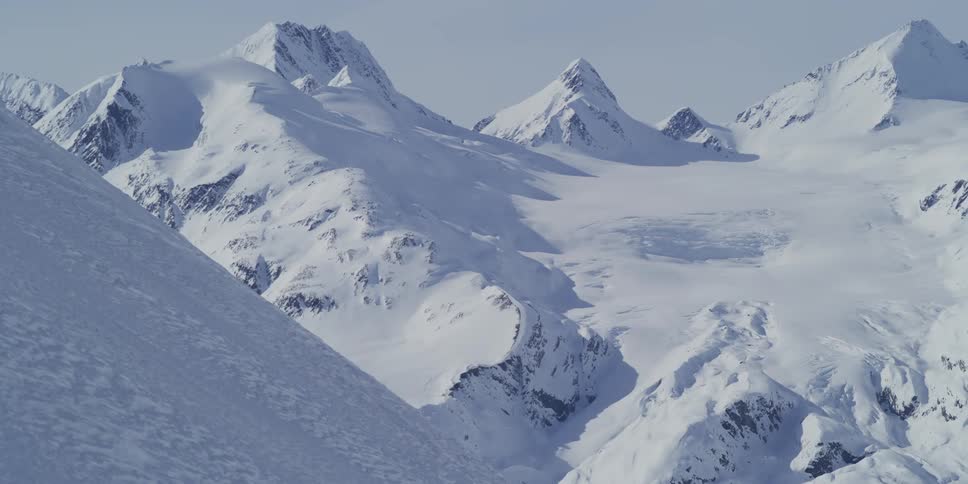 A slow panoramic reveal of a breathtakingly vast and untouched snow-covered mountain range under a clear sky