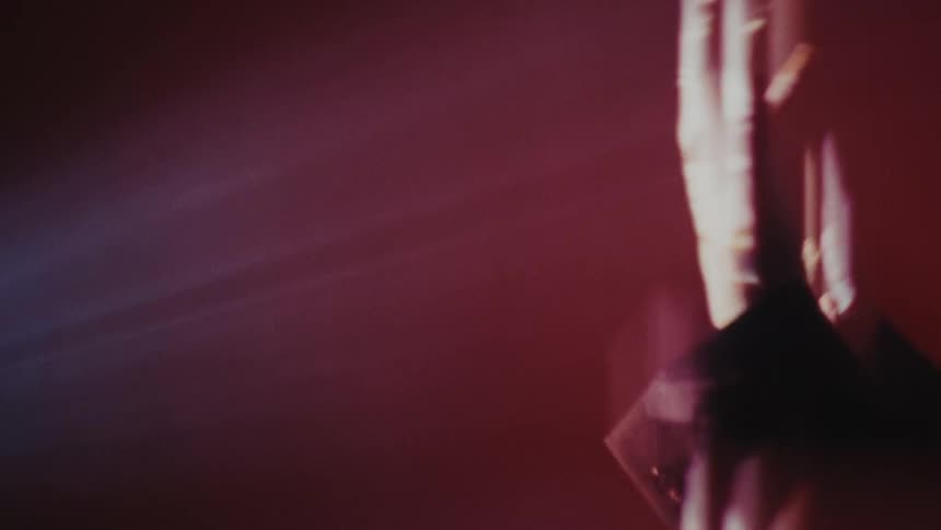 An abstract, dreamlike shot of a person's hand holding a glass, with light refracting through it against a hazy red background