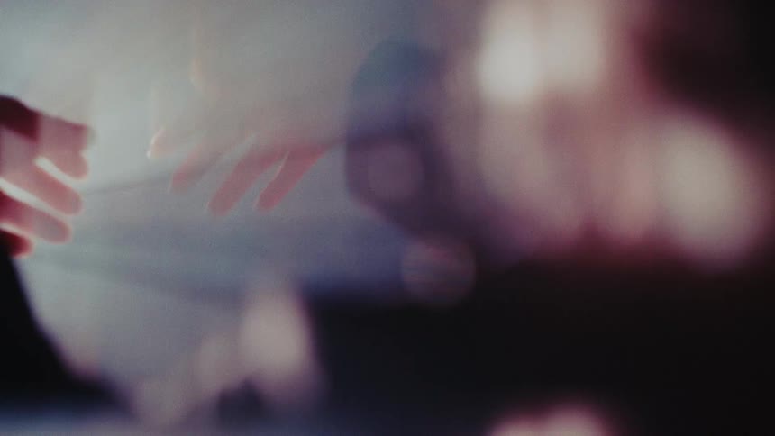 A person's silhouetted hands reach up towards a bright, hazy light source, creating dreamy and colorful lens flares