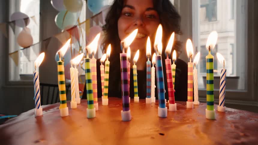A happy woman smiles as she blows out the colorful candles on her birthday cake in slow motion