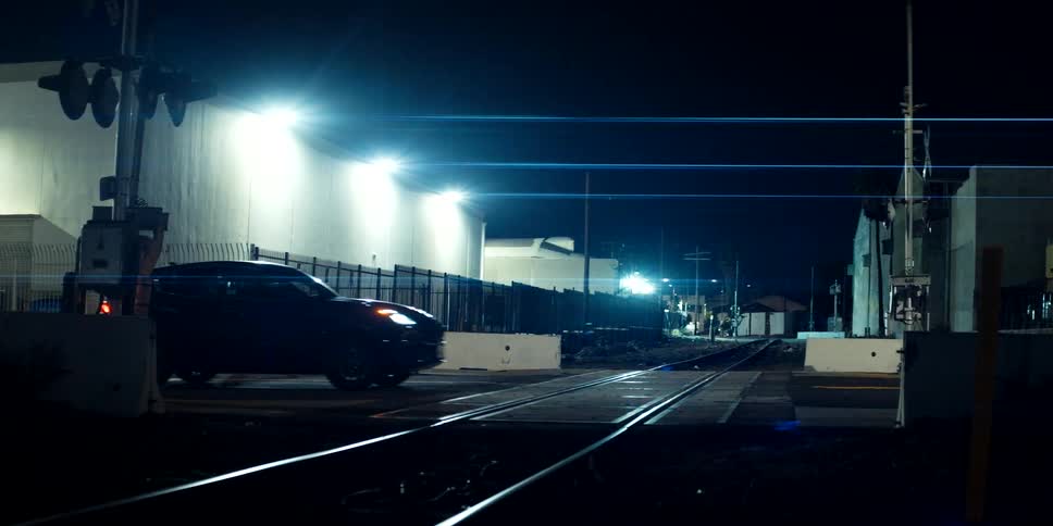 A dark SUV stops on the train tracks at night while the red warning lights flash