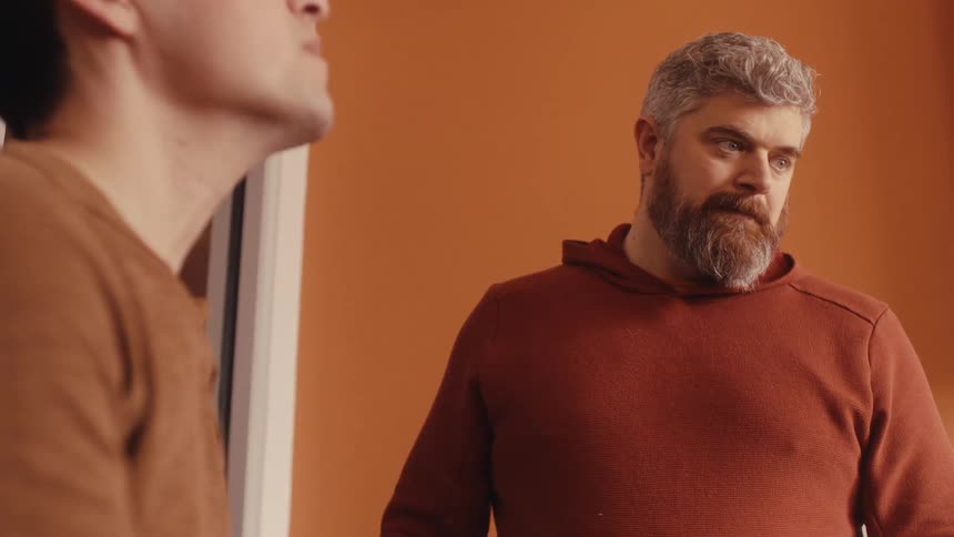 A middle-aged father with a grey beard listens with a serious and concerned expression as he has a difficult conversation with his son