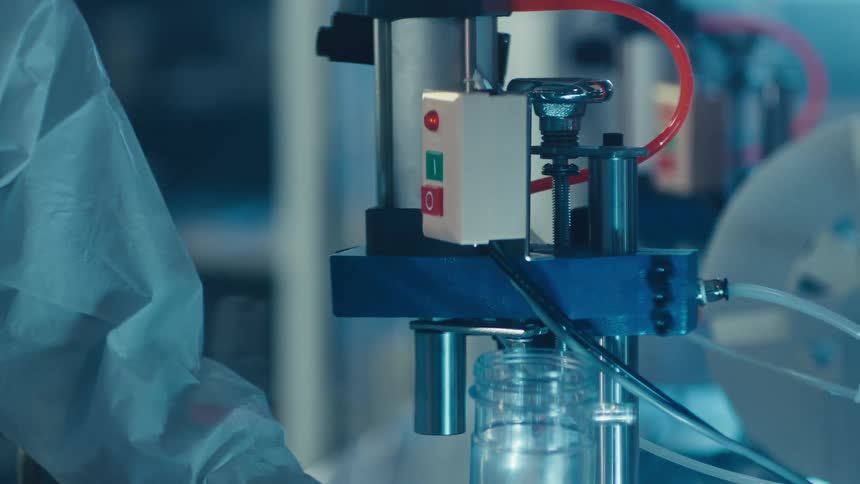 Close-up of a pneumatic machine automatically sealing a plastic jar in a factory