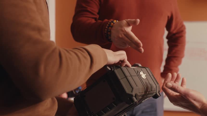 A bearded man in a hoodie explains the features of a rugged case to his younger colleague in a slow-motion close-up