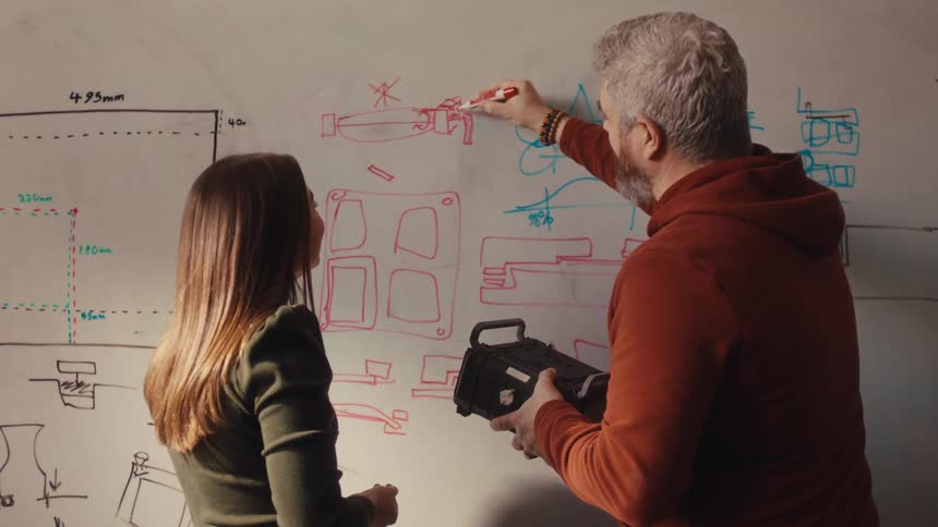 Two designers collaborate on a product idea, discussing sketches and plans on a whiteboard in their creative studio