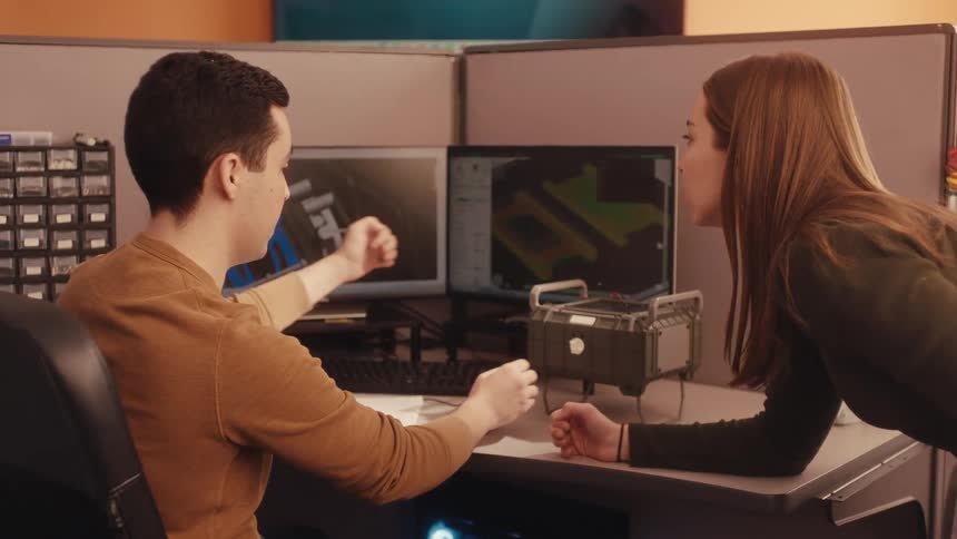 Two engineers collaborate on a new product design, comparing the 3D CAD model on the computer with a physical prototype