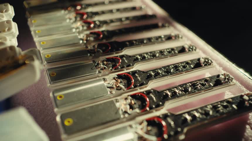 A close-up slow pan over a row of unfinished electronic components with exposed wiring on a production line