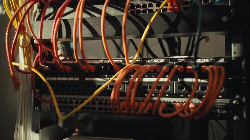 A dramatic close-up of tangled orange and yellow Ethernet cables plugged into a network server rack