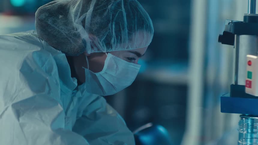 A female researcher in a full protective suit and mask meticulously operates scientific equipment in a sterile, modern laboratory