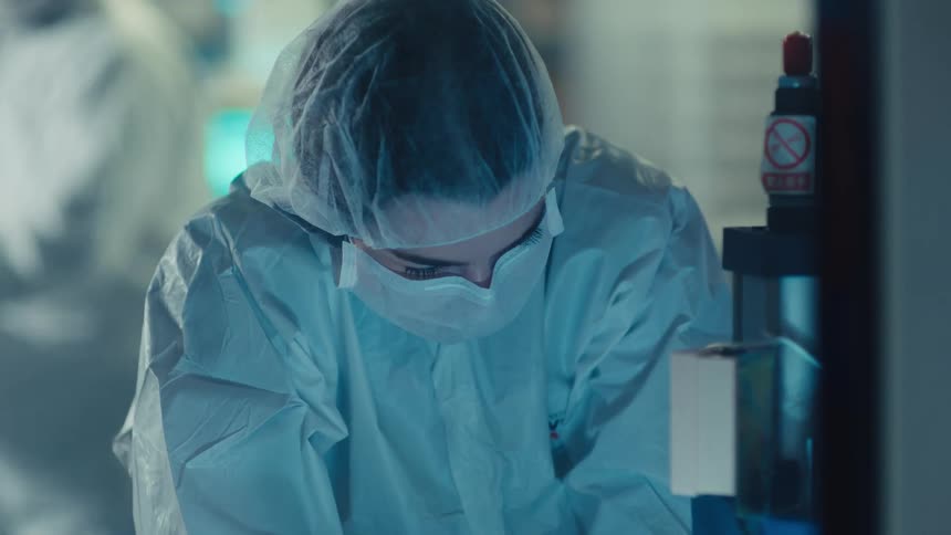 A focused scientist in a sterile protective suit works in a modern laboratory before walking away from her station
