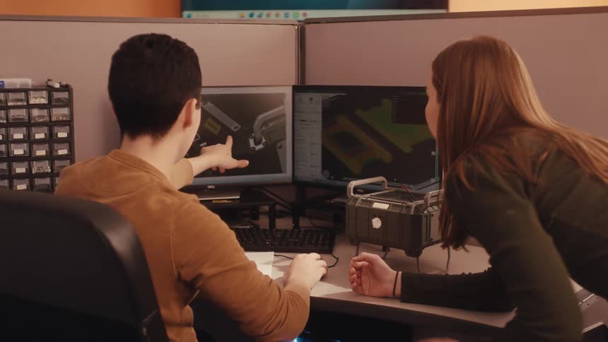 Two engineers collaborate on a product design, comparing the 3D CAD model on their computer to a physical prototype
