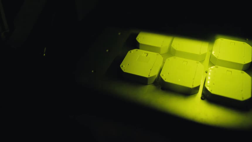 An industrial machine uses a yellow light beam to process white plastic components on a dark assembly line