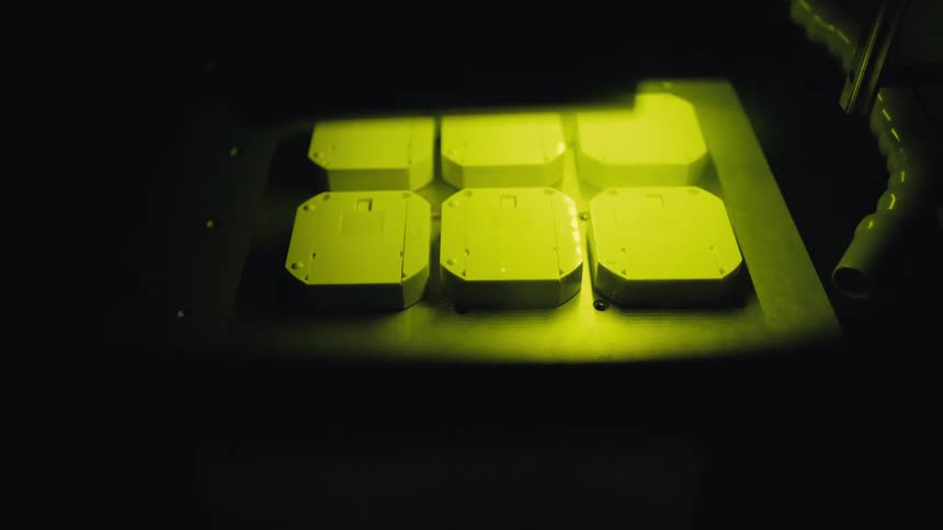 An automated machine scans over a tray of white electronic components with a beam of yellow light