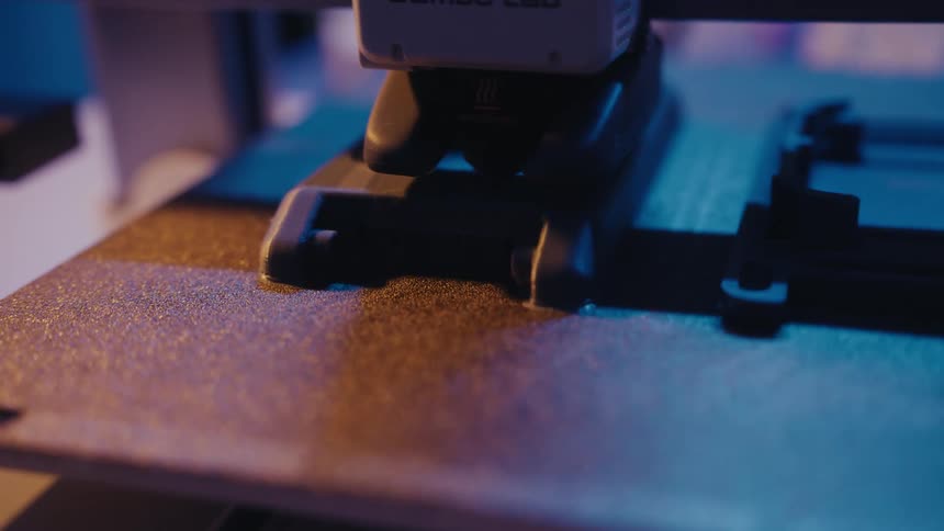 Close-up of a high-tech 3D printer head moving precisely as it creates a black plastic object layer by layer