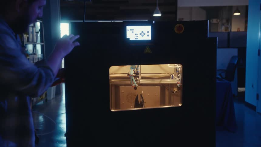 A male engineer opens a large 3D printer and removes a newly created futuristic model in a modern workshop