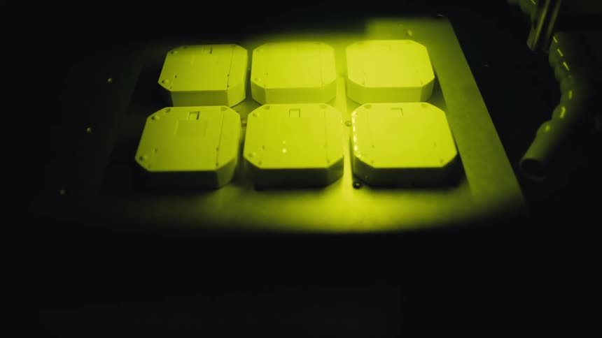 A close-up of an automated laser marking machine precisely engraving details onto white plastic components in a dark workshop
