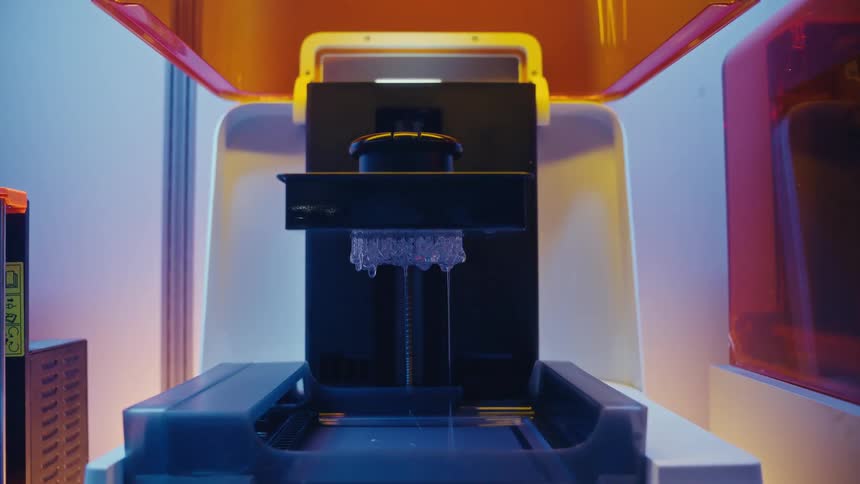 A stereolithography 3D printer lifts a newly printed translucent object out of a vat of liquid resin