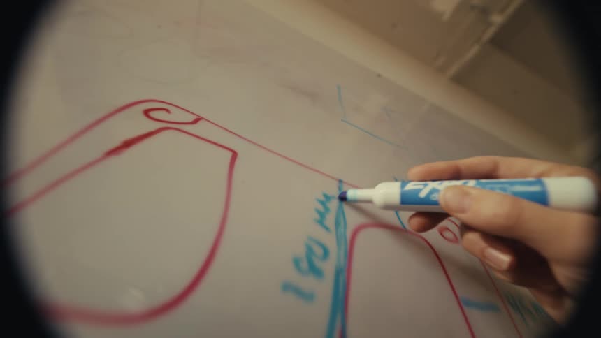 A designer's hand carefully sketches product schematics on a whiteboard in a creative POV shot
