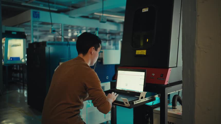 A young technician sets up and operates a CNC laser cutting machine in a modern manufacturing workshop