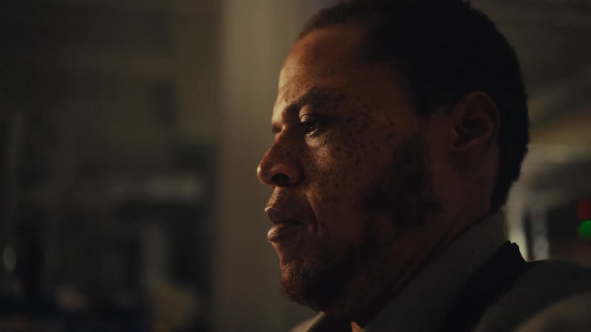 A close-up profile of a pensive Black man in a dimly lit, warm room
