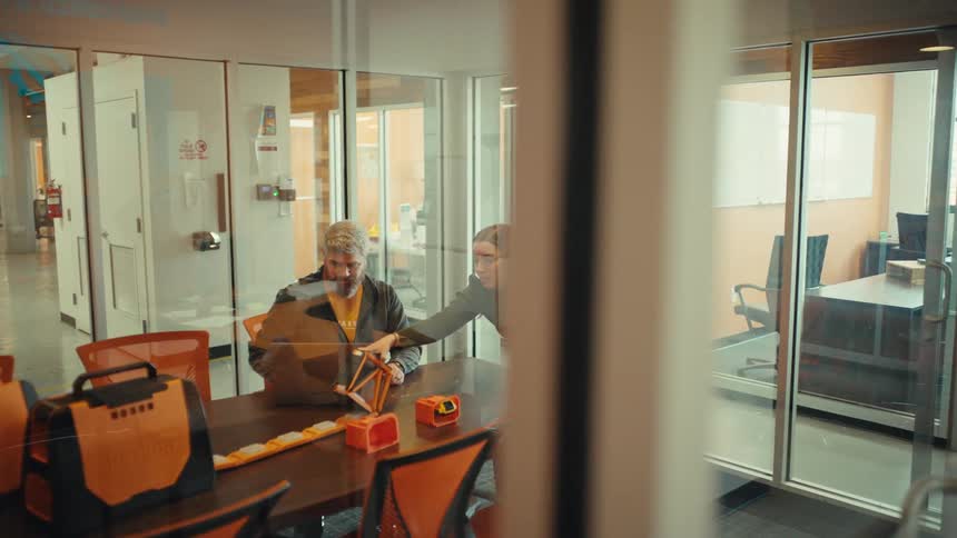 A man and woman collaborate on a new product design, examining prototypes in a modern glass-walled conference room