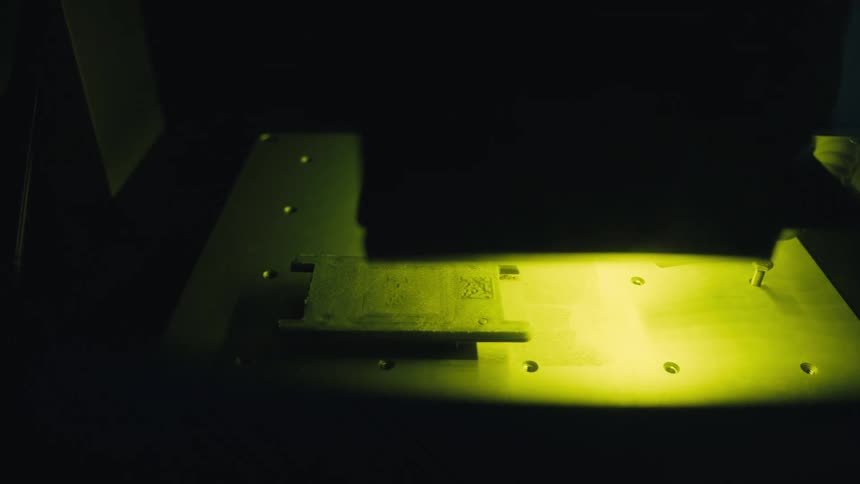 A laser marking machine precisely engraves a QR code and logo onto a metal plate in a dark industrial setting