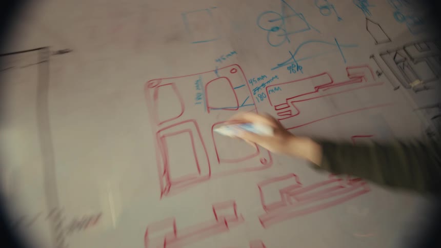A female designer or engineer meticulously sketches technical drawings with precise measurements onto a whiteboard