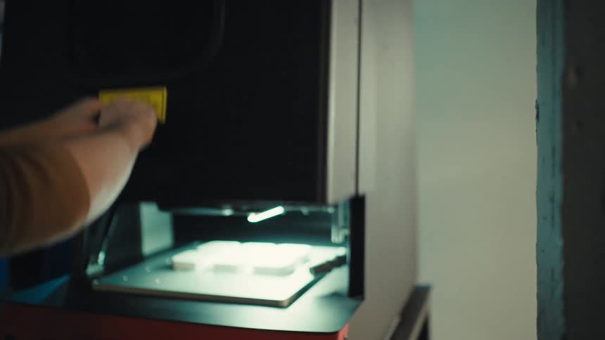 A young man operates an industrial laser cutter, placing a warning label on the door and programming it with a laptop in a modern factory