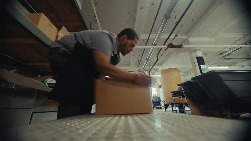Low-angle time-lapse of an industrial worker grabbing boxes off a shelf and packing them onto a rolling cart