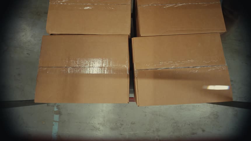POV shot from a dolly as a warehouse worker stacks and transports cardboard boxes
