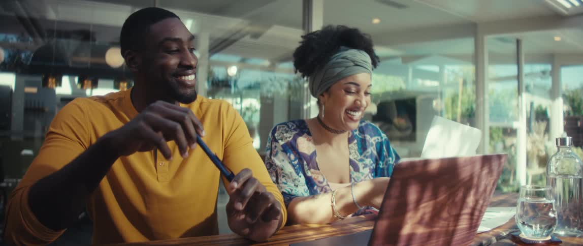 A joyful young couple collaborates on a project, laughing as they review paperwork and work on a laptop in a bright, modern room