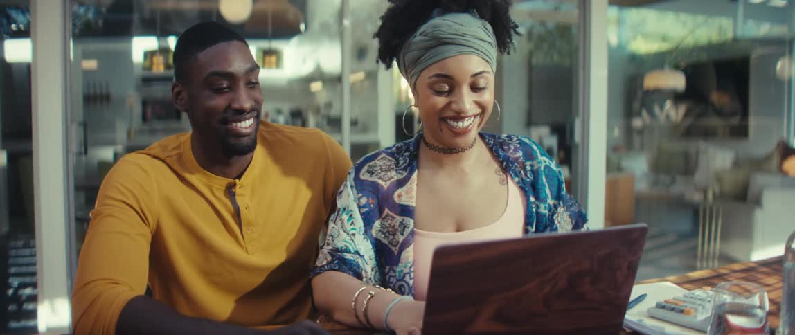 A happy young couple works together on a laptop, smiling and laughing in their modern home