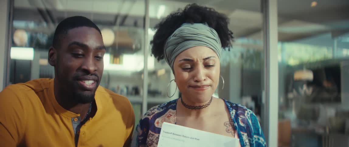 A young man and woman laugh joyfully while reviewing business performance charts on a laptop in a sunlit modern space