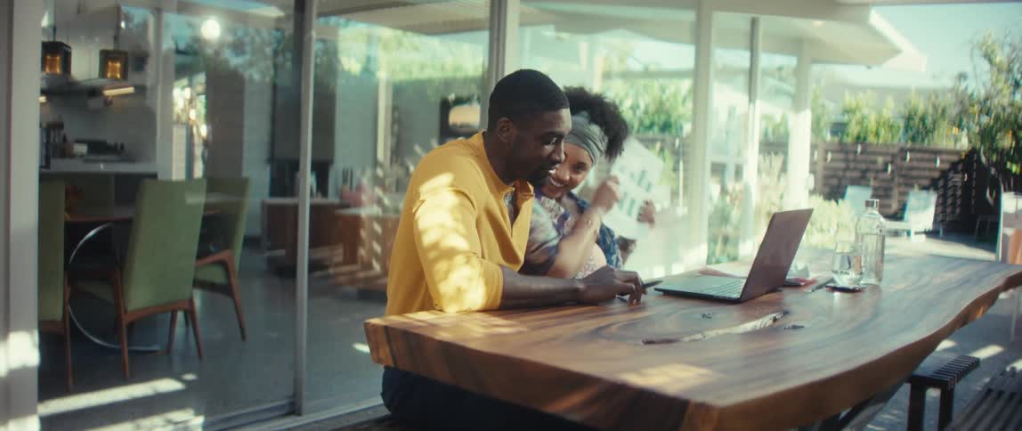 A happy couple works together from their modern, sunlit home, reviewing charts on a laptop and paper