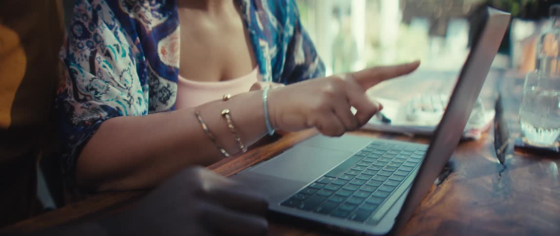 A young woman explains something on a laptop to her male colleague, pointing at the screen and typing on the keyboard