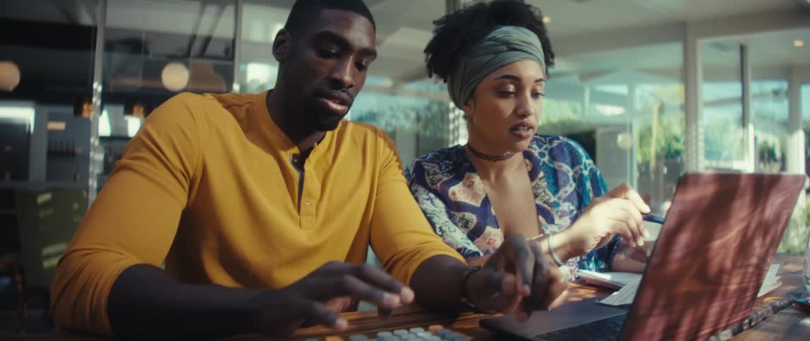 A young couple diligently calculates their finances together using a laptop and calculator in their sunlit modern home