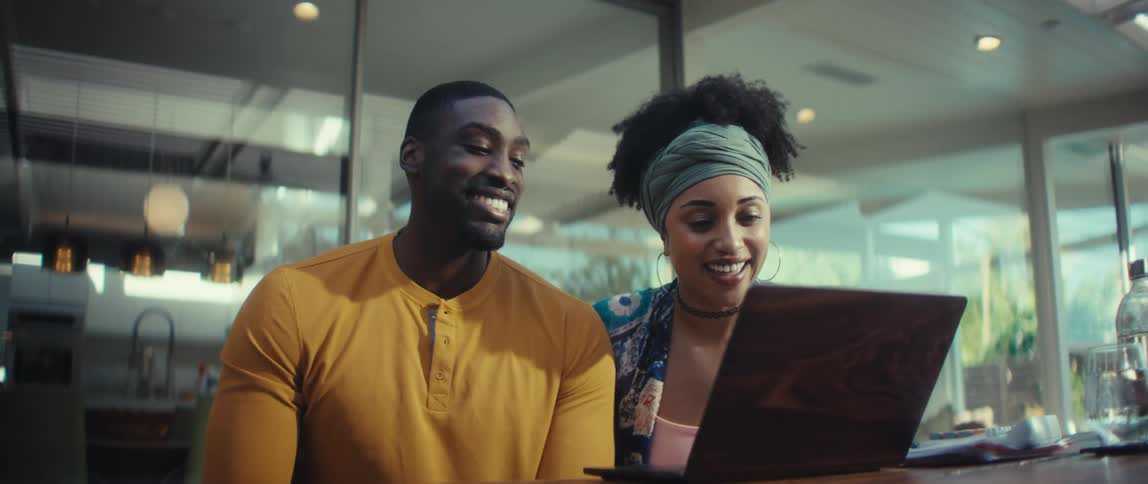 A joyous Black couple laughs together while on a video call on their laptop in a modern, sunlit room