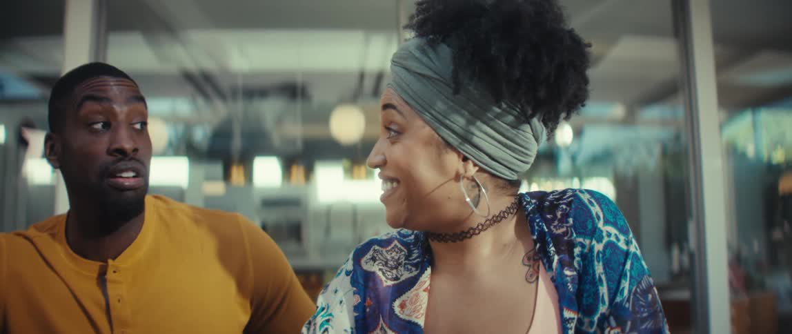 A young African American woman's expression shifts from focus to pure joy and laughter as she and a male friend watch something exciting on a laptop