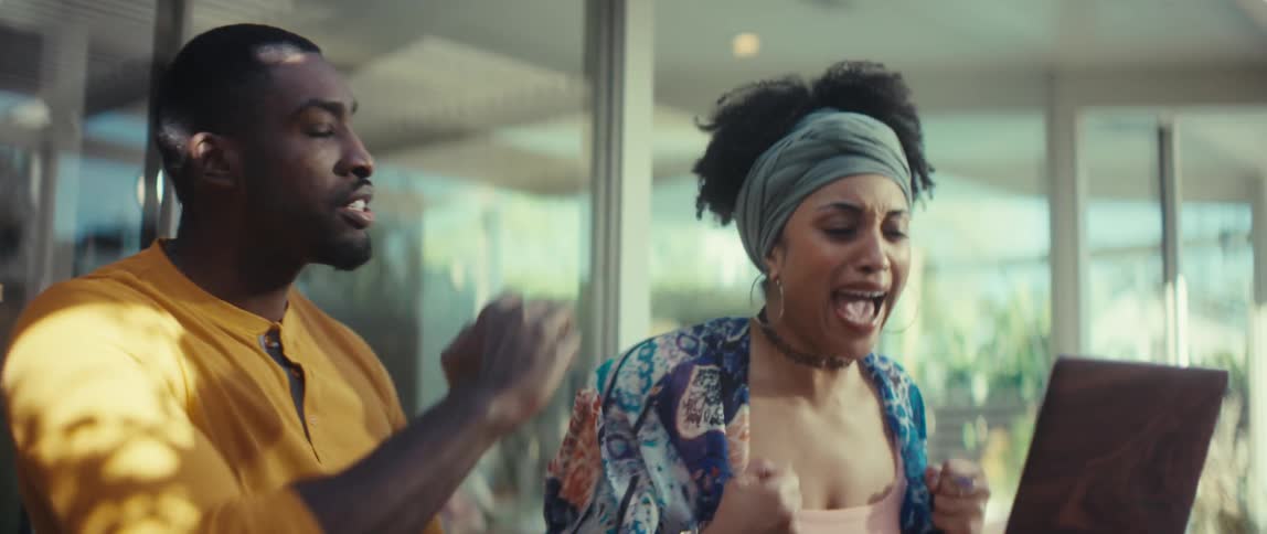 An ecstatic young couple celebrates great news on their laptop in super slow motion, cheering and giving each other a high five