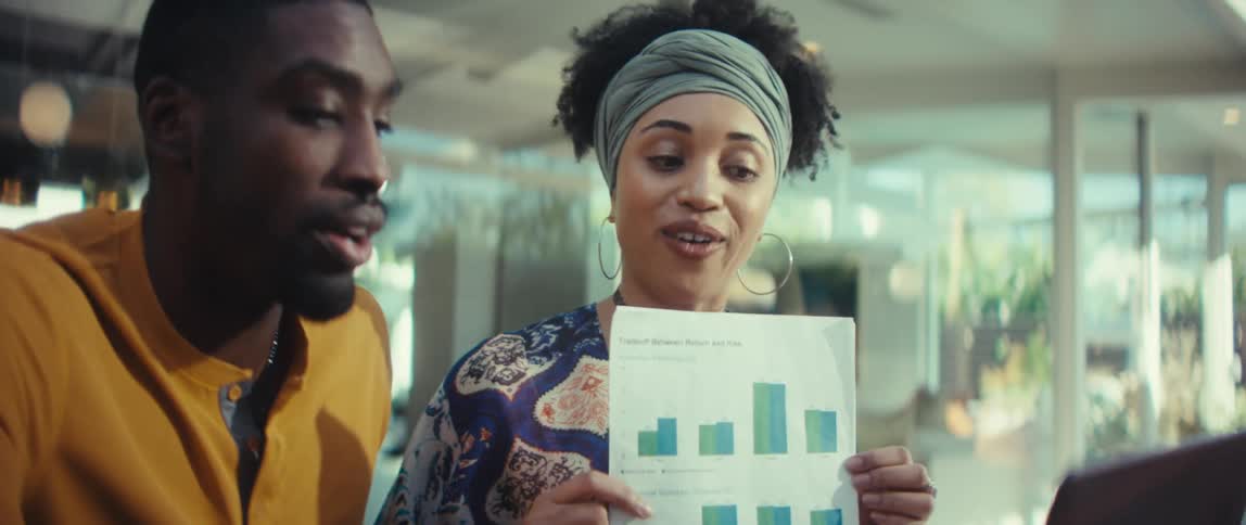 Two enthusiastic African American business partners discuss a successful project, analyzing a chart with positive results during a meeting in a bright office