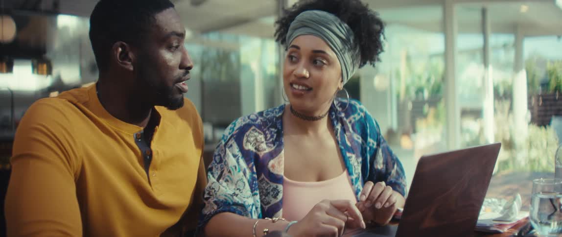 A young African American couple collaborates while looking at a laptop, animatedly discussing what's on the screen in their modern sunlit home